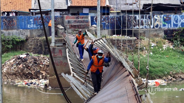 Sejumlah pekerja melintasi jembatan gantung yang rusak di aliran Kanal Banjir Barat (KBB), Grogol Petamburan, Jakarta Barat, Minggu (31/8/2014). Jembatan gantung yang nyaris amburk sejak sekitar 3 bulan yang lalu itu, kini tengah diperbaiki. Warga sekitar berharap perbaikan itu segera selesai. Warta Kota/angga bhagya nugraha