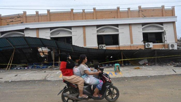 Pengendara sepeda motor melintas di depan bangunan berlantai dua yang runtuh akibat gempa berkekuatan 6,2 SR di Mamuju. Foto direkam Minggu (17/1/2021).