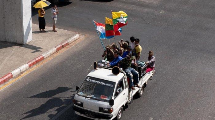 Pejalan kaki menyaksikan para pendukung militer memegang bendera nasional dan tentara sambil meneriakkan slogan-slogan saat mereka mengambil bagian dalam unjuk rasa di Yangon pada 1 Februari 2021