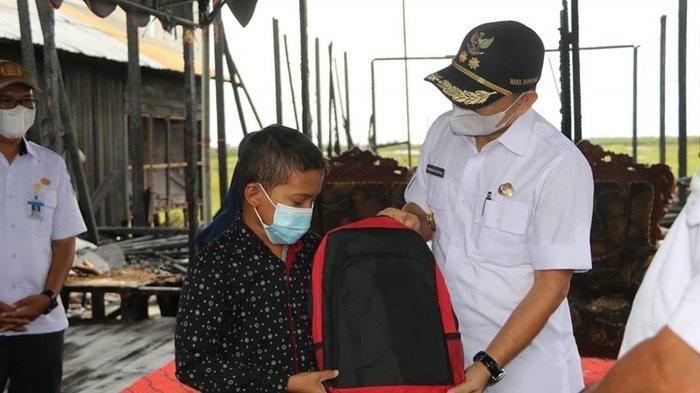 Wakil Bupati Syamsuri Arsyad menyerahkan perlengkapan sekolah kepad seorang anak yang rumahnya terbakar di Desa Bajayau Tengah RT 02 RW 02, Kecamatan Daha Barat, Kabupaten Hulu Sungai Selatan (HSS), Provinsi Kalimantan Selatan, Rabu (19/5/2021).