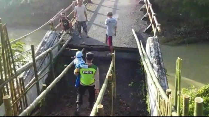 Bhabinkamtibmas Polsek Jatilawang menggendong anak sekolah menyeberang jembatan yang putus di atas Sungai Lopasir di Desa Karanglewas, Kecamatan Jatilawang, Senin (28/11/2022). Bersama warga, mereka membantu anak-anak sekolah menyeberang jembatan saat berangkat dan pulang sekolah.