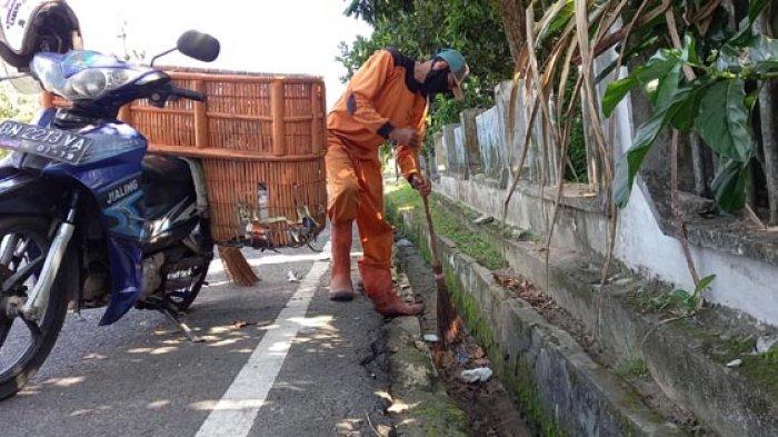 Petugas kebersihan menyapu sampah di drainase.