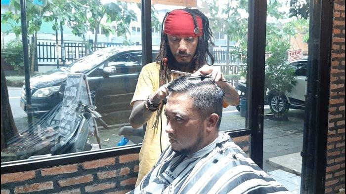 Diding yang berpenampilan seperti Jack Sparrow saat mencukur rambut konsumennya di Jack Dink's Barbershop & Dreadlock, Jalan Perjuangan, Kota Cirebon, Sabtu (6/3/2021).