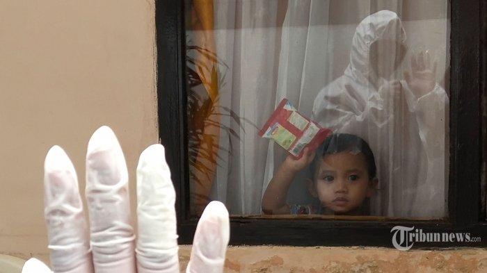 ILUSTRASI Isolasi Mandiri Anak -- FOTO: Kader PKK, Lia Nur Jauharatul Mardiah (42) mengenakan APD baju hazmat melambaikan tangan kepada anak kecil dari balik kaca jendela saat membawa makanan untuk dibagikan kepada warga yang terpapar Covid-19 di Gang Cisitu Lama 1, RW 11, Kelurahan Dago, Kecamatan Coblong, Kota Bandung, Jawa Barat, Senin (22/2/2021). Langkah proaktif yang dilakukan pengurus dan kader PKK RW 11 membagikan makanan kepada warga yang sedang melakukan isolasi mandiri ini sebagai kebersamaan saling membantu dalam menangkal penyebaran Covid-19. Selain itu, warga juga membatasi akses jalan gang dan mendirikan posko Covid-19 selama pemberlakuan pembatasan kegiatan masyarakat (PPKM).