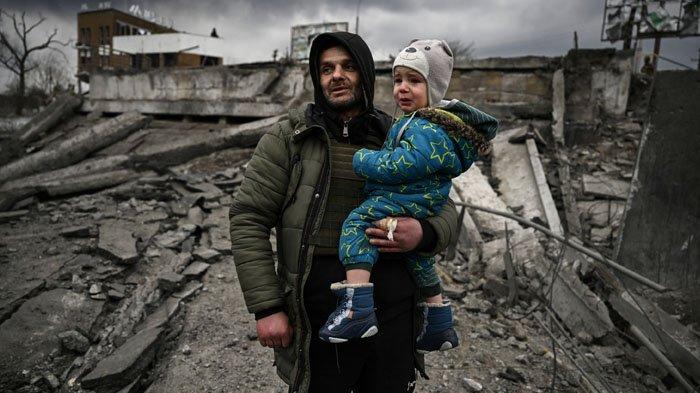 Seorang pria menggendong bocah di tengah reruntuhan rumah di Irpin, barat Kiev Ukraina, akibat pengeboman terus menerus oleh Rusia, Senin (7/3/2022). Rusia mengajukan empat syarat untuk menghentikan serangan militernya.