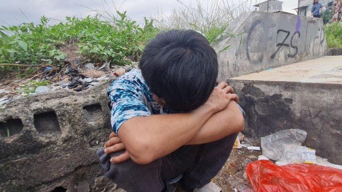 Japra (20) duduk berjongkok sembari menunduk di sebuah lahan kosong di Kampung Boncos, Palmerah, Jakarta Barat pada Kamis (1/12/2022).