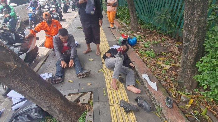 Pengendara motor berinisial J (kiri/duduk) dan penumpangnya berinisial NA (kanan/tiduran) berada di trotoar Jalan Gatot Subroto depan JCC usai mengalami kecelakaan lalu lintas pada Kamis (6/10/2022).