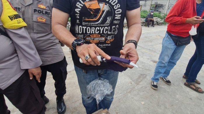 Anggota buru sergap (buser) membalut pisau yang diduga beracun menggunakan kain saat penggerebekan narkoba di Kampung Boncos, Palmerah, Jakarta Barat, Kamis (1/12/2022).