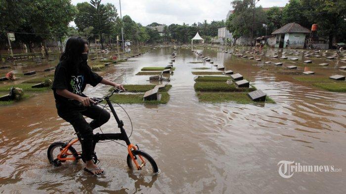 Warga bersepeda melintas di tengah makam yang terendam banjir di TPU Jeruk Purut, Jakarta Selatan, Sabtu (20/2/2021). Pemerintah Provinsi (Pemprov) DKI Jakarta dinilai tidak siap menanggulangi banjir yang terjadi dalam sepekan terakhir.