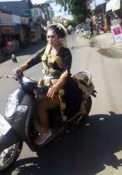 Wanita yang memakai pakaian pengantin adat Jawa mengendarai motor sendiri dan melintasi jalan raya.