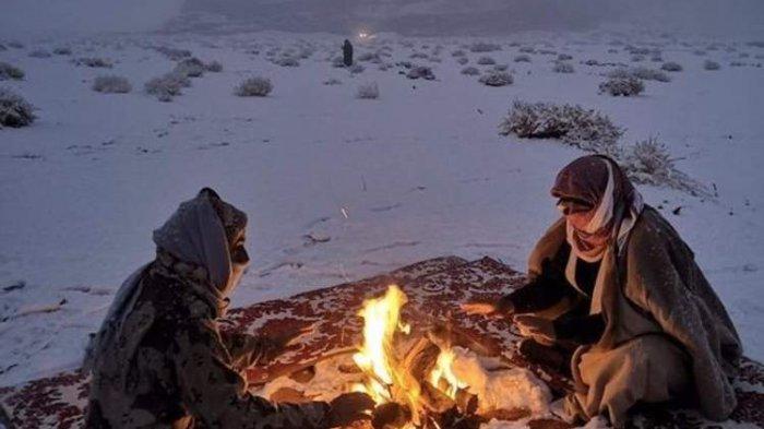 Warga Tabuk, Arab Saudi, menghangatkan diri di perapian di tengah turunnya salju. Wilayah padang pasir tandus ini mengalami musim salju hingga beberapa minggu ke depan.