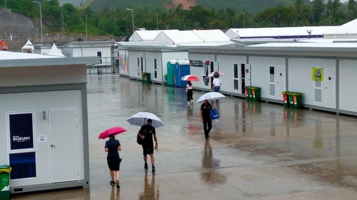 Para kru MotoGP memakai payung saat berjalan di area belakang paddock Sirkuit Mandalika, Sabtu 19 Maret 2022.