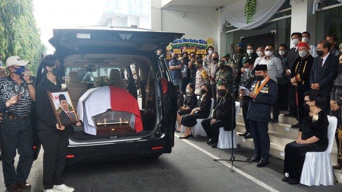 Sebastian cucu mendiang Sarundajang anak dari Vanda Sarundajang memegang erat foto opa-nya di belakang mobil jenazah