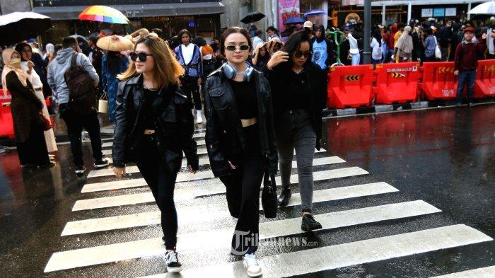 Bak seorang model profesional seorang pengunjung memamerkan pakaian yang menarik dan nyentrik sambil membuat konten media sosial bergaya berjalan di atas zebra cross di acara