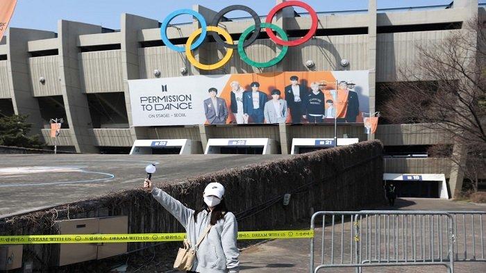 Seorang wanita berpose untuk foto di depan spanduk besar yang menunjukkan anggota grup K-pop BTS di Stadion Olimpiade Jamsil di Seoul pada 9 Maret 2022, menjelang konser langsung grup tersebut di stadion pada 10, 12 dan 13 Maret.