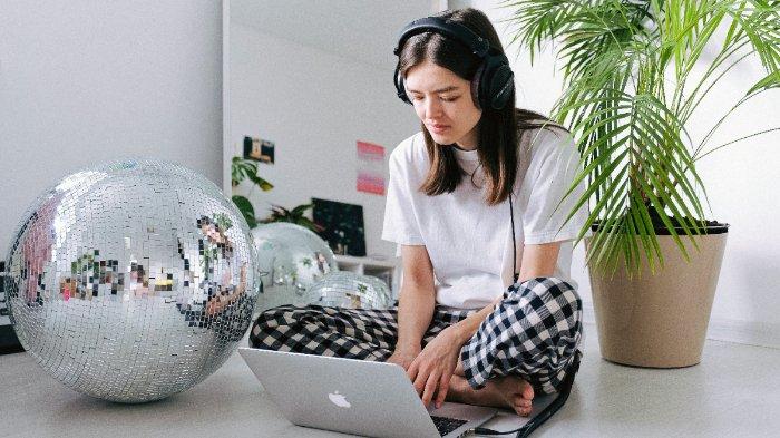 Ilustrasi perempuan memakai headphone saat menggunakan laptop.