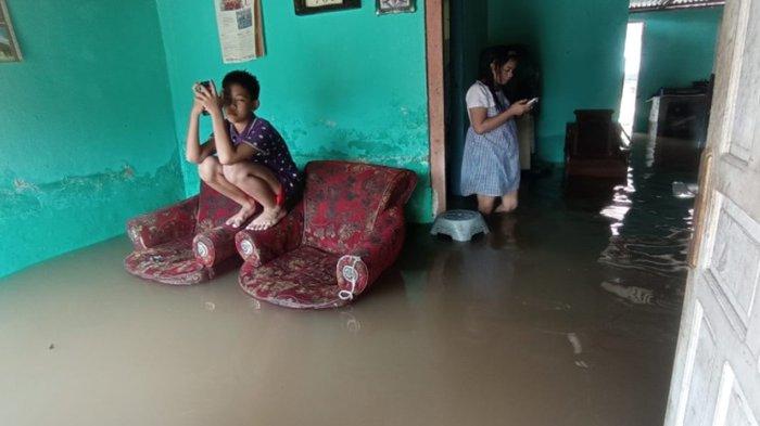 Dua orang anak terlihat tetap asyik main gadgetnya di saat kediaman mereka di kawasan Kemang Manis Palembang kebanjiran, Sabtu (25/12/2021).