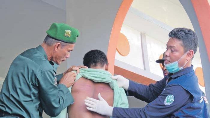 Petugas medis memeriksa punggung terpidana kasus masir (judi) yang lebam-lebam berwarna merah bekas cambukan saat menjalani ekseskusi cambuk di Alun-alun Suka Makmue, Nagan Raya, Jumat (13/3/2020).