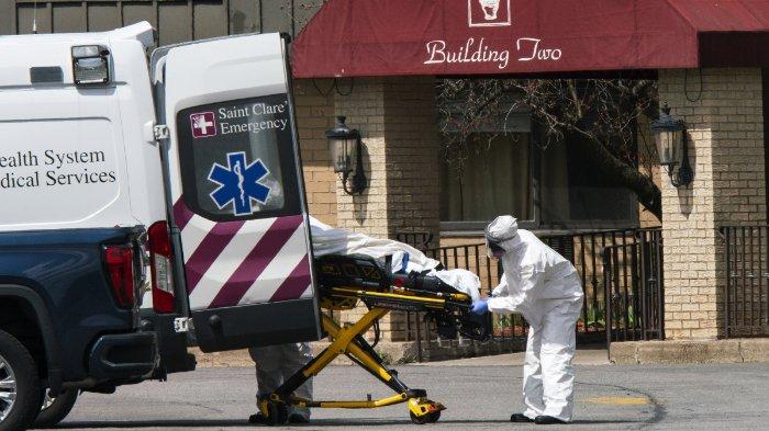 Pekerja medis memasukkan mayat ke dalam ambulans sambil mengenakan masker dan alat pelindung diri (APD) di Pusat Subakut dan Rehabilitasi Andover pada 16 April 2020 di Andover, New Jersey. Setelah mendapatkan laporan anonim di kepolisian, 17 orang ditemukan tewas di fasilitas perawatan jangka panjang, termasuk dua perawat, di mana setidaknya 76 pasien dan 41 anggota staf telah dinyatakan positif COVID-19.