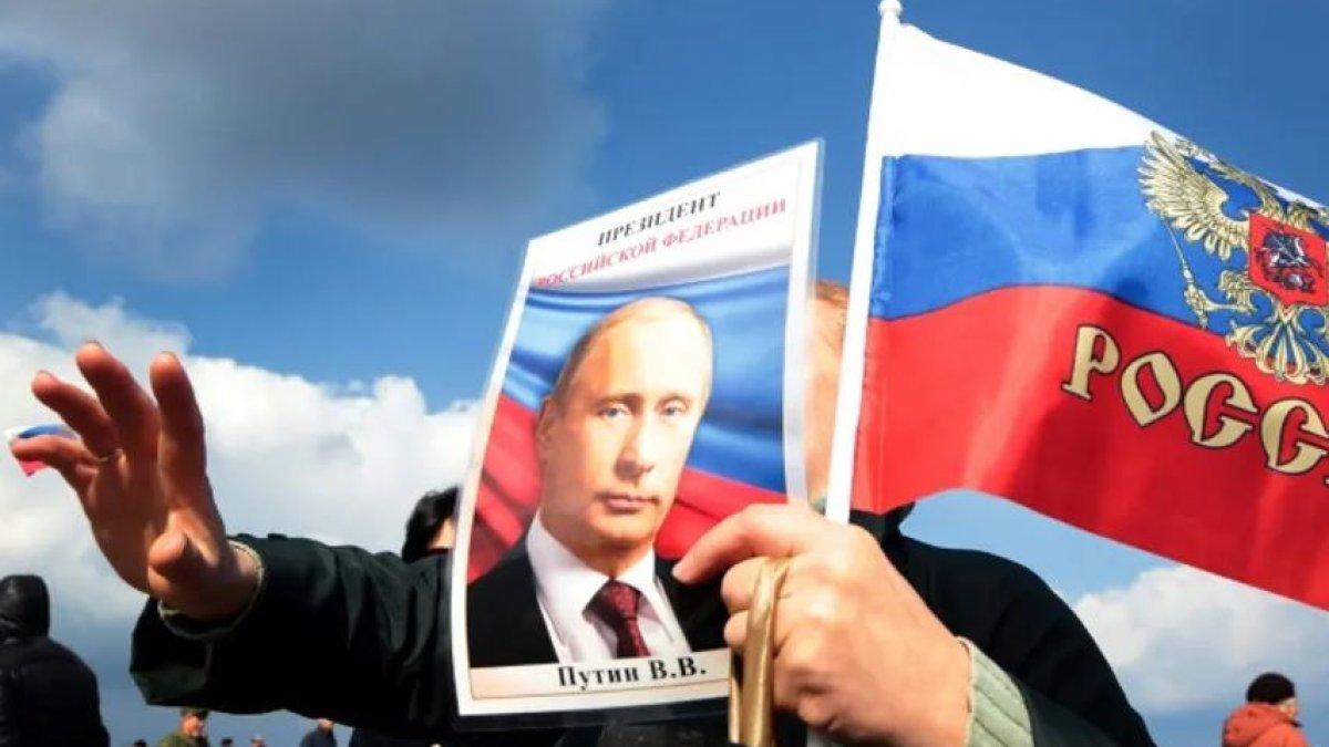 Seorang demonstran mengibarkan bendera nasional Rusia dan potret Presiden Vladimir Putin dalam perayaan ulang tahun ketiga pencaplokan Krimea oleh Rusia, di Sevastopol pada Maret 2017.
